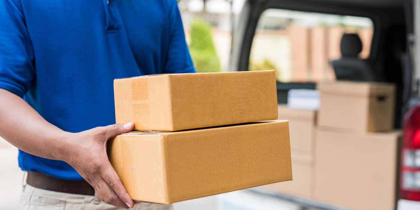 Delivery professional holding two stacked cardboard packages, showcasing final mile e-commerce fulfillment from a delivery vehicle