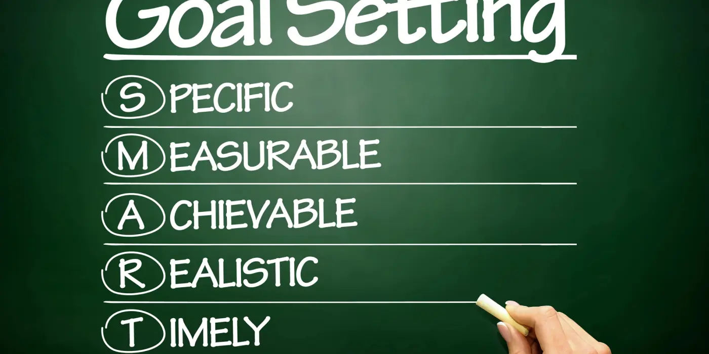 Hand writing the SMART acronym on a green chalkboard to outline delivery management software implementation goals